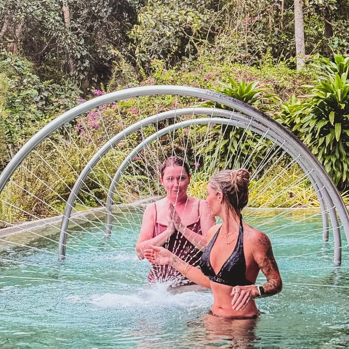 Two women in a spring-fed pool under arched water jets at The Farm at San Benito